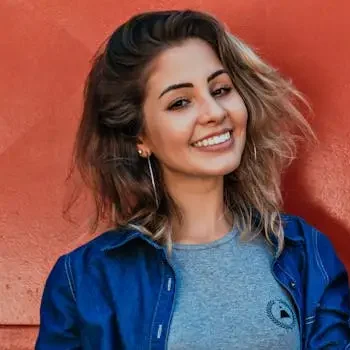 A woman in a denim jacket smiling brightly against a vibrant red and blue background.